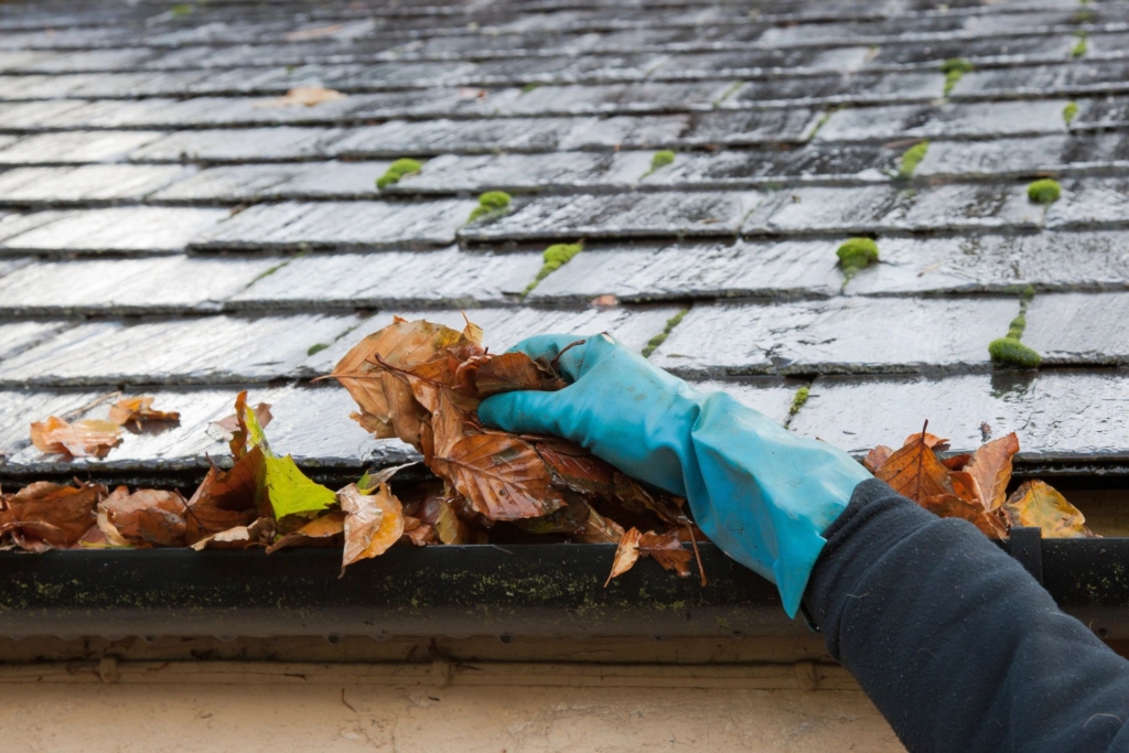 A hand cleaning leaves from a gutter